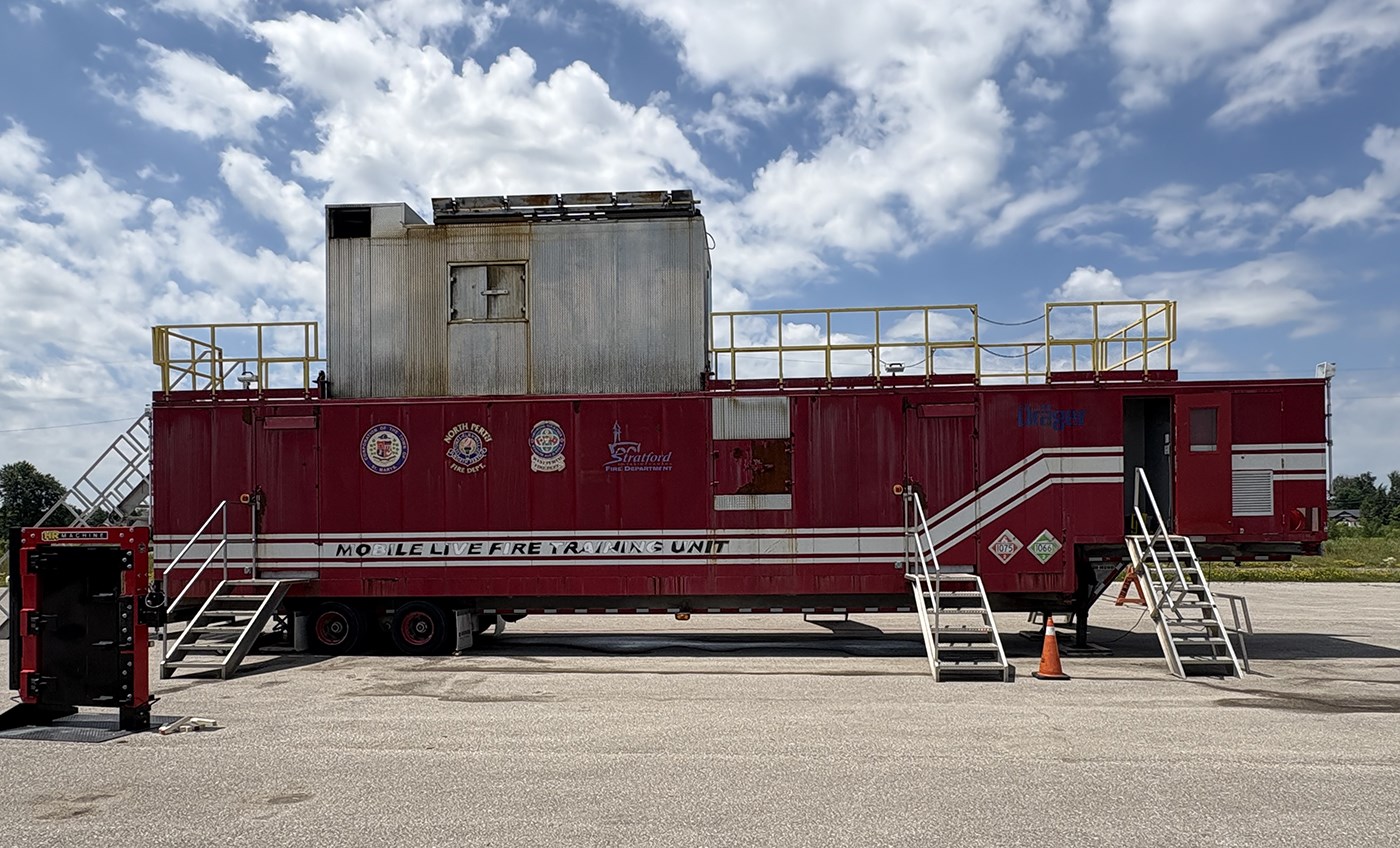 A red coloured mobile fire training unit trailer in a parking lot.
