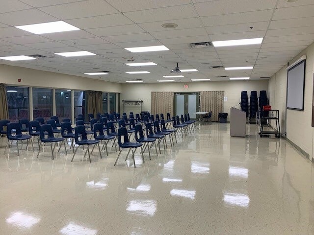 A large meeting room with empty chairs facing a screen and podium.