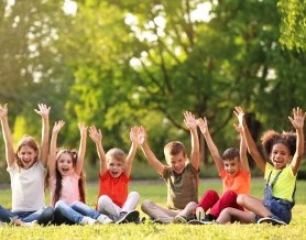 Children in a park, sitting on the grass and raising their hands