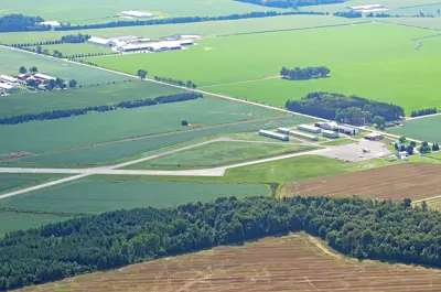 An airport building and runways surrounded by green fields and trees