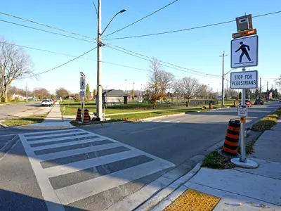A city intersection with a pedestrian crossover, showing painted stripes on the road and signage