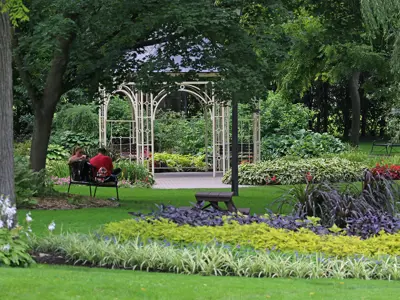 A gazebo in the middle of a park with trees and colourful flowerbeds