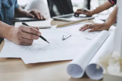 Blueprints on a table, with hands pointing to them