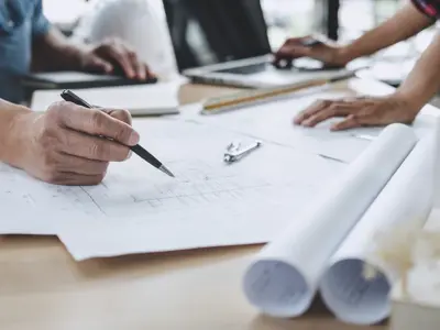 Blueprints on a table, with hands pointing to them