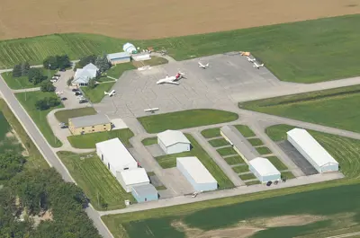 An airport building with planes on the asphalt, with runways surrounded by green fields and trees