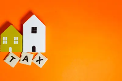 Two small model homes above letter tiles spelling TAX on orange background
